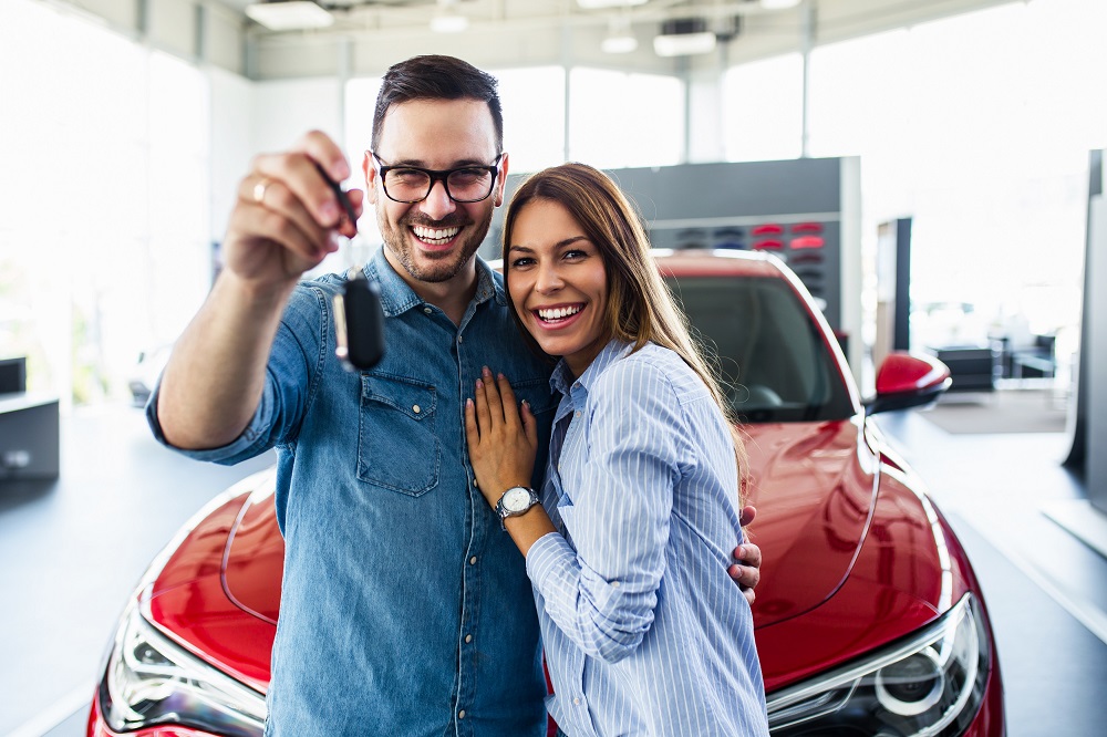Beautiful young smiling couple holding a key of their new car.